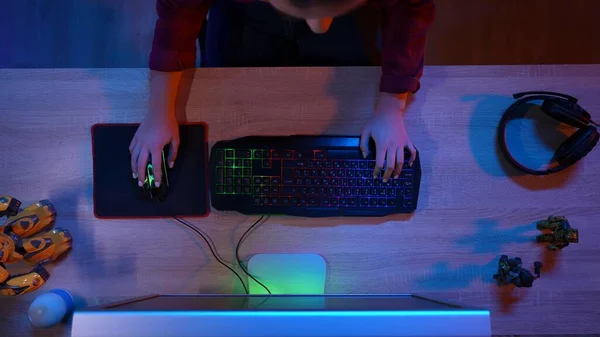 Online gaming advertisement concept. Blogger gamer at the PC at home. Top view close up girl sitting at the desk playing action game on computer online, hands on keyboard.