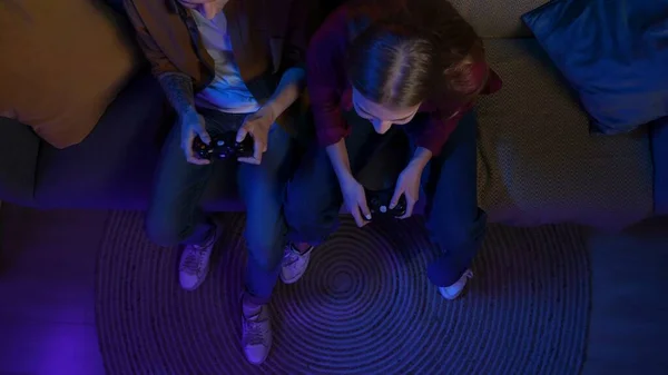 Online gaming and entertainment concept. People spending free time at home. Top view close up of couple sitting on the sofa in the living room, playing action video game on TV .