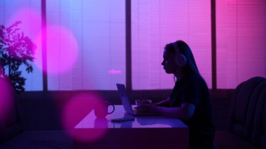 Günlük hayat ve insan ilişkileri kavramı. Kafeteryadaki kişinin portresi. Geceleri neon ışıkta yemek büfesinde oturan, kulaklık takan, dizüstü bilgisayarla çalışan bir kızın silueti..