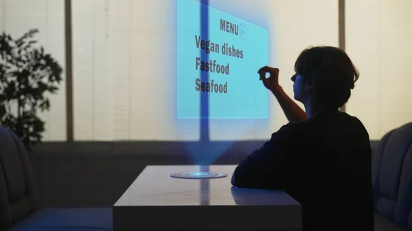 Person in cafeteria. Silhouette of man at the fast food bistro bar is using virtual reality menu picking meals. Selection of vegan dishes, fast food, seafood. Menu hologram, computer graphics, screen