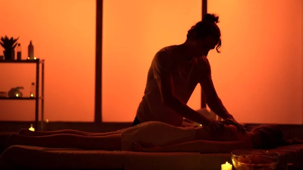 Masseur, massage specialist giving back massage to his patient. Silhouettes in the massaging room, spa procedure. Exotic, orange neon lights. Healthcare, medical treatment, holistic therapy.
