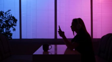 Günlük yaşam sosyal ilişkiler siluet konsepti. Kafeteryadaki kadın portresi. Gece fast food barında oturan, kulaklık takan, akıllı telefondan müzik dinleyen bir kız..