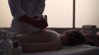 Masör, masaj uzmanı, bitkisel poşetler kullanarak hastasına masaj yapıyor. Masaj odasında bir kadınla bir erkeğin siluetleri, spa prosedürü. Sağlık, tıbbi tedavi, bütünsel terapi.
