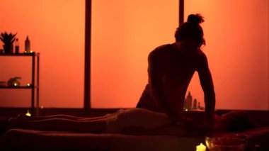 Masör, masaj uzmanı hastasına el ve kol masajı yapıyor. Masaj odasında siluetler, spa prosedürü. Egzotik, turuncu neon ışıklar. Sağlık, tıbbi tedavi, bütünsel terapi.