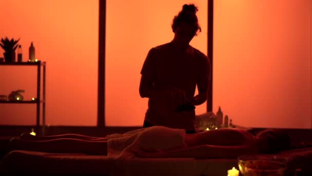 按摩师 按摩师 用加热的石头进行轻松的按摩 按摩室 温泉疗程的轮廓 奇异的橙色霓虹灯保健 综合治疗 — 图库视频影像