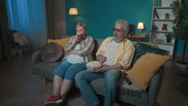 ショットでは 高齢のカップルがソファーに座って映画を見たり テレビでショーしたり ポップコーンを食べたりしています 彼らは笑って どうやらコメディを見ているようだ ハッピーで 楽しいわ 一般プラン — ストック動画
