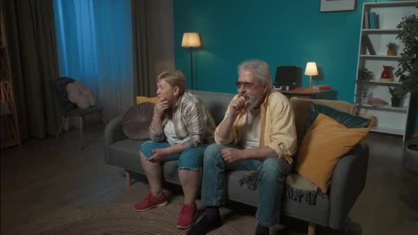 年配のカップルが部屋のソファーに座り どこかをじっと見つめていた 彼らは興奮し 何かを待っている それから彼らは喜び始める 満足を実証する — ストック動画