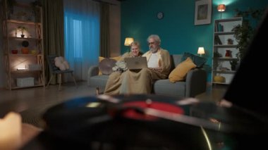 Kapalı çekim, dönen diski olan vinil bir plak çaları gösteriyor. Yaşlı bir çift bir kanepede dizüstü bilgisayarla oturuyor ve video iletişimi yoluyla birileriyle konuşuyor. Gülümseyip el sallıyorlar..