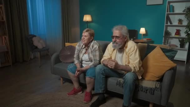 年配のカップルが部屋のソファーに座り どこかをじっと見つめていた 彼らは興奮し 何かを待っている すると彼らは怒り 悲しみ 悲しみを実証する — ストック動画