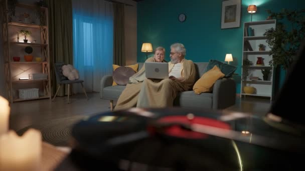クローズアップ画像は 回転ディスクを持つビニールレコードプレーヤーを示しています 背景には 高齢のカップルがラップトップとサーフィンウェブサイトとソーシャルメディアでソファーに座っています ミディアムビデオ — ストック動画