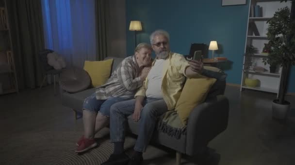 写真では 高齢のカップルがアパートのソファーに座っています 男は携帯電話を持っていて 彼らはセルフィーのためにポーズします その男はその女性にその写真を見せた Hdr Bt2020 Hlg材料について — ストック動画