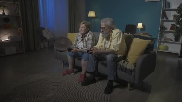 写真では 高齢のカップルがアパートのソファーに座っています 彼らは情熱的に 競争し 話し合い 相互に干渉するビデオゲームをプレイします 女性は幸せで 男性は動揺しています Hdr Bt2020 — ストック動画