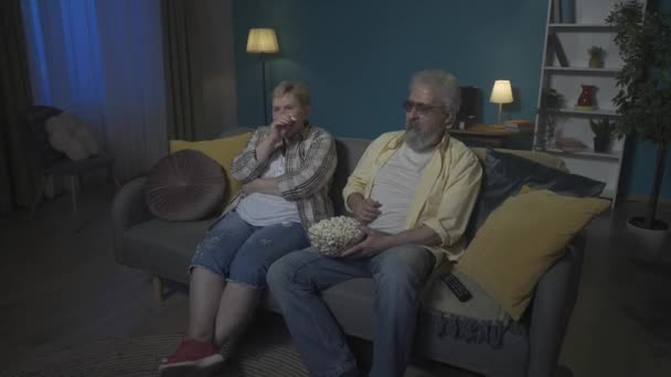 ショットでは 高齢のカップルがソファーに座って映画を見たり テレビでショーしたり ポップコーンを食べたりしています 彼らは笑って どうやらコメディを見ているようだ Hdr Bt2020 Hlg材料について — ストック動画