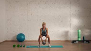 Evde kişisel spor eğitimleri. Spor giyimli bir kadın spor yapıyor. Sağlık ve sağlık reklamları konsepti. Atletik kadın fitness koçu kettlebell tarafı ve ön tarafı ile çömelme hareketleri yapıyor..