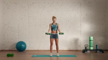 Evde kişisel spor eğitimleri. Spor giyimli bir kadın spor yapıyor. Sağlık ve sağlık reklamları konsepti. Atletik kadın fitness koçu dambıllarla biseps kaldırma yapıyor, online dersler..