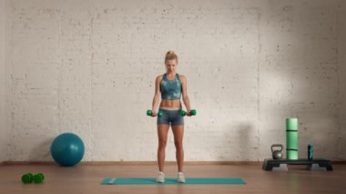 Evde kişisel spor eğitimleri. Spor giyimli bir kadın spor yapıyor. Sağlık ve sağlık reklamları konsepti. Atletik kadın fitness koçu yan görüş pazılarını halterle kaldırıyor..