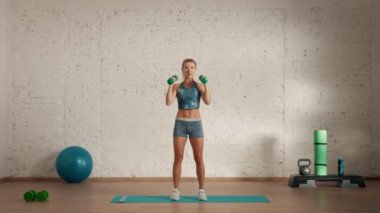 Evde kişisel spor eğitimleri. Spor giyimli bir kadın spor yapıyor. Sağlık ve sağlık reklamları konsepti. Atletik kadın fitness koçu çevrimiçi dersler için halterlerle kollarını kaldırıyor..