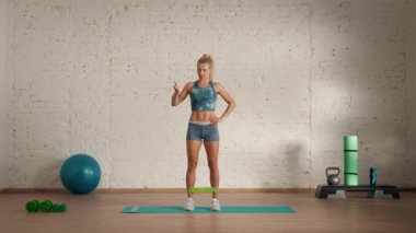 Evde kişisel spor eğitimleri. Spor giyimli bir kadın spor yapıyor. Sağlık ve sağlık reklamları konsepti. Atletik kadın fitness koçu kauçuk bantla yan bacak kaldırma yapıyor, online dersler