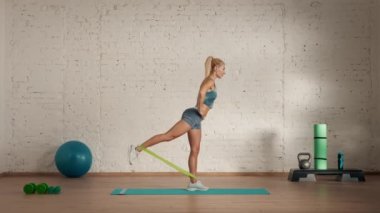 Evde kişisel spor eğitimleri. Spor giyimli bir kadın spor yapıyor. Sağlık ve sağlık reklamları konsepti. Atletik kadın fitness koçu sınıflar için lastik bantla arka bacak kaldırma yapıyor..