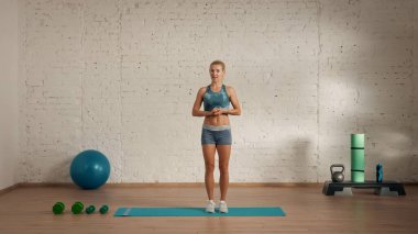 Evde online olarak kişisel spor dersleri. Spor giyim bölümünde egzersiz yapan sarışın bir kadın. Sağlık hizmetleri yaratıcı reklam konsepti. Kadın fitness koçu odada kameraya bakıyor, ayakta duruyor..