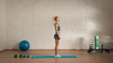 Evde online olarak kişisel spor dersleri. Spor giyim bölümünde egzersiz yapan sarışın bir kadın. Sağlık hizmetleri yaratıcı reklam konsepti. Kadın fitness koçu odada yoga minderinde dikiliyor..