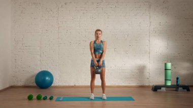 Evde online olarak kişisel spor dersleri. Spor giyim bölümünde egzersiz yapan sarışın bir kadın. Sağlık hizmetleri yaratıcı reklam konsepti. Kadın fitness koçu kettlebell düz elleriyle odada duruyor..