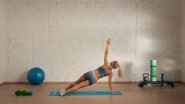 Evde online olarak kişisel spor dersleri. Spor giyim bölümünde egzersiz yapan sarışın bir kadın. Sağlık hizmetleri yaratıcı reklam konsepti. Kadın fitness koçu salonda, vücut çevirme tahtası yapıyor..