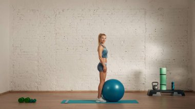 Evde online olarak kişisel spor dersleri. Spor giyim bölümünde egzersiz yapan sarışın bir kadın. Sağlık hizmetleri yaratıcı reklam konsepti. Kadın fitness koçu odada, elinde topla kameranın karşısında duruyor..