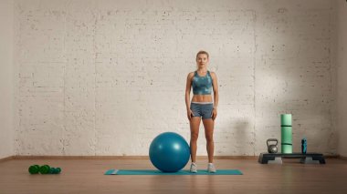 Evde online olarak kişisel spor dersleri. Spor giyim bölümünde egzersiz yapan sarışın bir kadın. Sağlık hizmetleri yaratıcı reklam konsepti. Odadaki kadın fitness koçu kameraya top gibi poz veriyor..