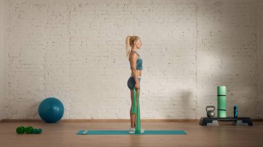 Evde online olarak kişisel spor dersleri. Spor giyim bölümünde egzersiz yapan sarışın bir kadın. Sağlık hizmetleri yaratıcı reklam konsepti. Kadın fitness koçu lastik bant kolunu kaldırıyor..