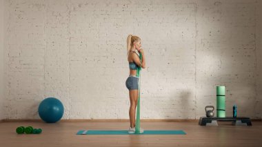 Evde online olarak kişisel spor dersleri. Spor giyim bölümünde egzersiz yapan sarışın bir kadın. Sağlık hizmetleri yaratıcı reklam konsepti. Kadın fitness koçu kauçuk bantla biceps yapıyor..