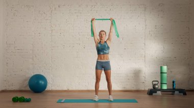 Evde online olarak kişisel spor dersleri. Spor giyim bölümünde egzersiz yapan sarışın bir kadın. Sağlık hizmetleri yaratıcı reklam konsepti. Kadın fitness koçu kauçuk bant tutarak odada..