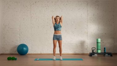 Evde online olarak kişisel spor dersleri. Spor giyim bölümünde egzersiz yapan sarışın bir kadın. Sağlık hizmetleri yaratıcı reklam konsepti. Kadın jimnastik koçu odada, arkasında dambıllar tutuyor..