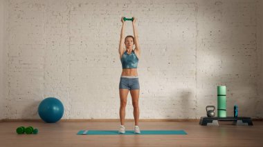 Evde online olarak kişisel spor dersleri. Spor giyim bölümünde egzersiz yapan sarışın bir kadın. Sağlık hizmetleri yaratıcı reklam konsepti. Kadın fitness koçu salonda, dambılı başının üstünde tutuyor. yukarı.