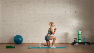 Evde online olarak kişisel spor dersleri. Spor giyim bölümünde egzersiz yapan sarışın bir kadın. Sağlık hizmetleri yaratıcı reklam konsepti. Kadın fitness koçu salonda, hafif hamleler yapıyor, yandan bakıyor..