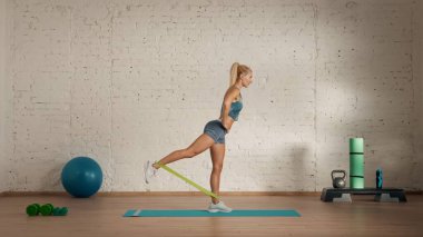 Evde online olarak kişisel spor dersleri. Spor giyim bölümünde egzersiz yapan sarışın bir kadın. Sağlık hizmetleri yaratıcı reklam konsepti. Kadın fitness koçu kauçuk bant bacağı kaldırıyor..