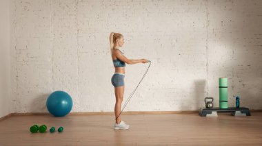 Evde online olarak kişisel spor dersleri. Spor giyim bölümünde egzersiz yapan sarışın bir kadın. Sağlık hizmetleri yaratıcı reklam konsepti. Odadaki kadın fitness koçu atlıyor ip atlıyor, yan görüş..