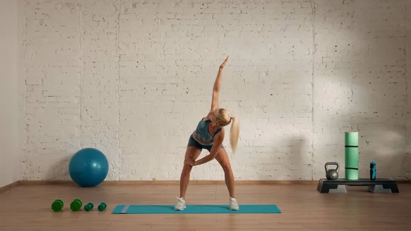 Personal sport classes at home online. Blonde female in sportswear doing exercises. Healthcare creative advertisement concept. Woman fitness coach in the room ding arm stretch to the top.