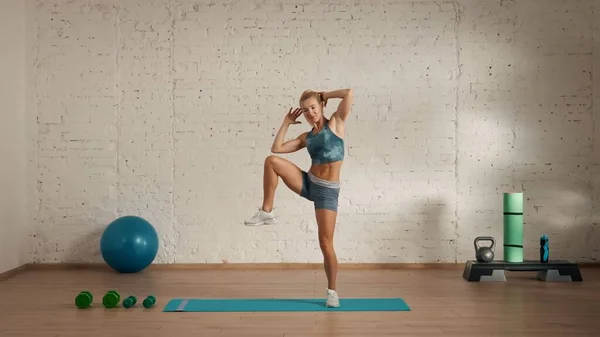 Personal sport classes at home online. Blonde female in sportswear doing exercises. Healthcare creative advertisement concept. Woman fitness coach in the room doing side knee rises.