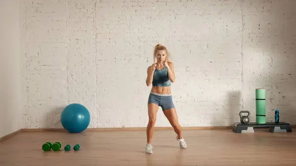 Personal sport classes at home online. Blonde female in sportswear doing exercises. Healthcare creative advertisement concept. Woman fitness coach in the room doing boxing exercise.