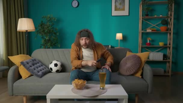 Mężczyzna Siedzi Kanapie Wyzywająco Ogląda Mecz Piłki Nożnej Telewizji Trzyma — Wideo stockowe