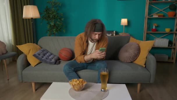 Homem Meia Idade Está Sentado Num Sofá Ele Segura Celular — Vídeo de Stock