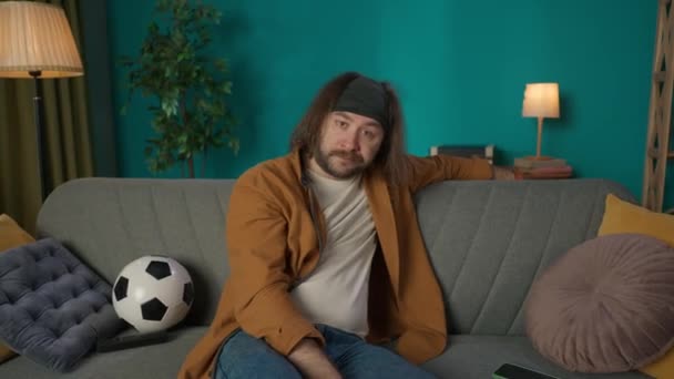 Homem Meia Idade Está Sentado Num Sofá Com Uma Bola — Vídeo de Stock
