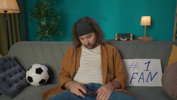 在镜头中 一个中年男人坐在沙发上打瞌睡 旁边躺着一个标志和一个球 他突然醒来 兴高采烈地喝啤酒 观看足球比赛的示威者 — 图库视频影像