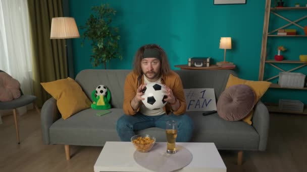 Kadrze Mężczyzna Średnim Wieku Siedzi Kanapie Ręku Piłkę Nożną Pokazuje — Wideo stockowe