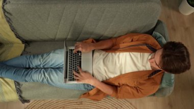 Kanepede uzanmış dizüstü bilgisayar ekranına bakan genç bir adamın görüntüsü. İnternette sohbet ediyormuş ya da sörf yapıyormuş gibi yazıyor. Boş zaman, online alışveriş, sosyal ağlar ve iletişim.