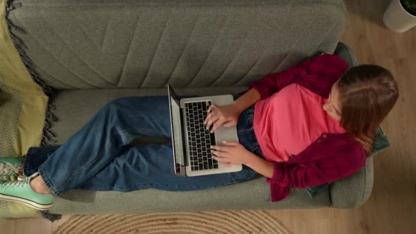 头像是一个年轻女人躺在沙发上 看着手提电脑屏幕 她打字时好像在聊天或上网 网上购物 社交网络和通信 — 图库视频影像