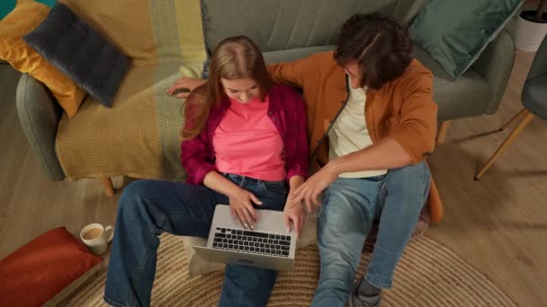 床に座っている若いカップルをキャプチャするトップビュー 抱きしめて話す 彼らがオンラインで何かを探しているかのようにラップトップ画面を見る レジャー オンラインショッピング ソーシャル — ストック動画