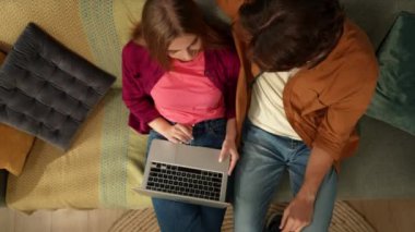Kanepede oturan, kucaklaşan ve konuşan genç bir çifti internette bir şey arıyormuş gibi dizüstü bilgisayar ekranına bakarken görüntülemek. Aile, eğlence, online alışveriş, sosyal
