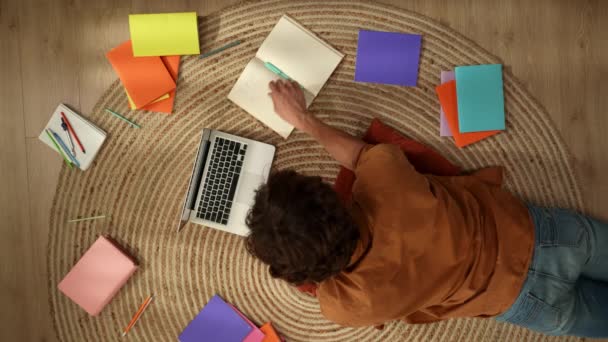 바닥에 공부하는 젊은이를 노트북에서 작업하고 메모를 다채로운 책으로 둘러싸여 Homeschooling — 비디오